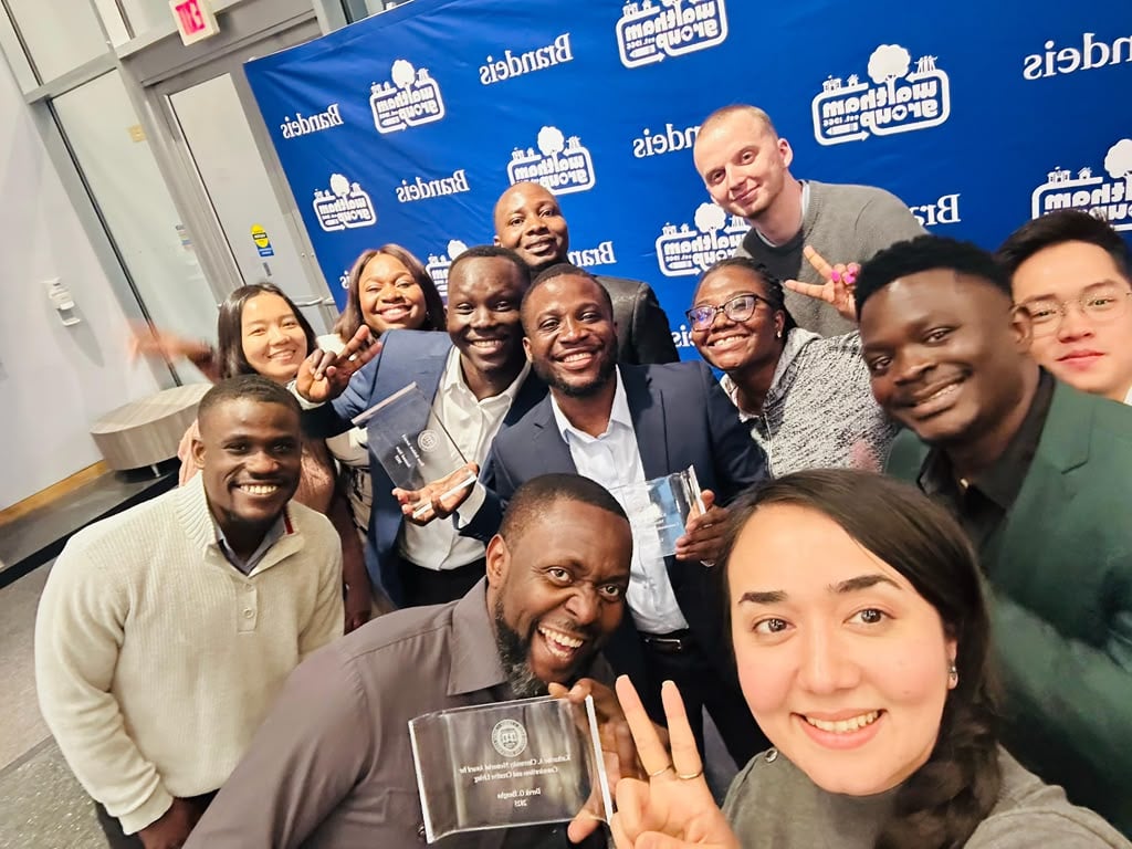 A group of students and staff celebrating together, holding glass awards at an evening ceremony