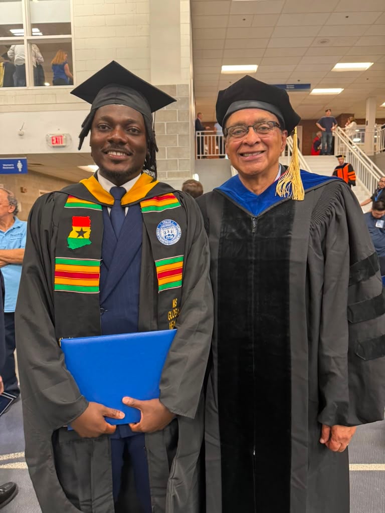 Terrick in graduation regalia with a Ghana kente stole, standing beside a faculty member in doctoral robes